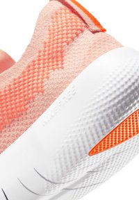 Heled roosa tennisjalanõud tekstuurse ülemise osaga, oranžide aktsentidega ja valge mustriga tallaga. "NIKE FREE" on küljele peale pressitud.