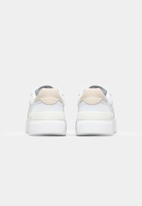 Fehér sneakers, sima bőrrel, szürke velúr díszítéssel és textúrált fehér gumitalppal. Lekerekített orral és párnázott bokarésszel rendelkezik.