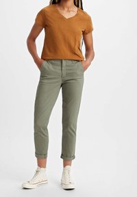 Brun V-ringad t-shirt, ljusgröna skräddarsydda byxor med upprullade ärmar, vita högskurna sneakers och raka ben. Enkel design, avslappnad stil.
