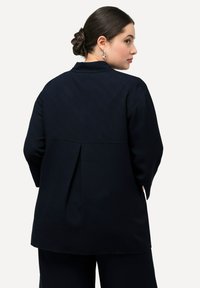Blazer navy con una vestibilità rilassata, dotato di colletto a punta, dettaglio sul retro plissettato e maniche lunghe. Realizzato in un tessuto liscio e strutturato.