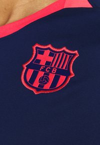 Marinblå sportströja med en framträdande broderad röd och blå FC Barcelona-logotyp som har vertikala ränder och en central cirkulär logotyp.