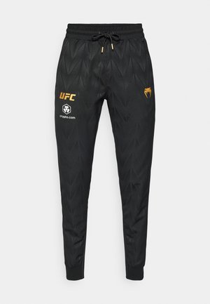 Μαύρο αθλητικό παντελόνι με υφή γεωμετρικού σχεδίου. Διαθέτει ελαστική ζώνη μέσης, κορδόνι και λογότυπα σε χρυσό και λευκό.