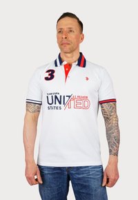 Bílá polo košile s červenými a tmavě modrými akcenty, s límcem a krátkými rukávy. Zobrazuje "3" a "UNITED STATES" v tučném písmu.