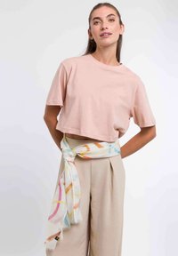 Light pink cropped t-shirt with short sleeves paired with beige high-waisted pants. A lightweight, multicolored patterned scarf is tied at the waist.