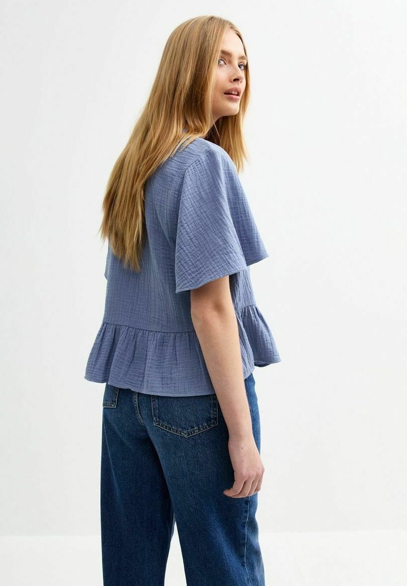 Ljusblå, texturerad kortärmad topp med peplum-söm, tillsammans med lösa mörkblå jeans. Toppen har en avslappnad passform och mjukt material.