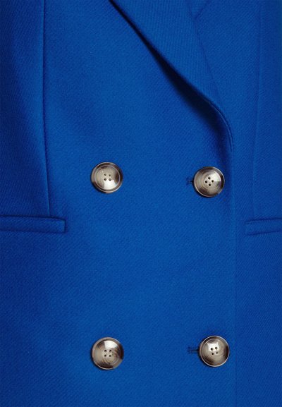 Blazer din lână albastră, cu design cu două rânduri de nasturi, rever cu tăietură în V și nasturi argintii cu patru găuri. Suprafață texturată, croi ajustat.