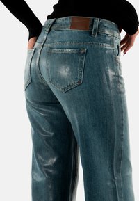 Vaqueros de mezclilla azul de talle alto con un ligero brillo, que cuentan con bolsillos traseros y una etiqueta de cuero en la cintura.