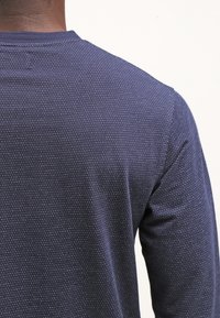 Navy long-sleeve shirt made of textured fabric featuring a subtle dotted pattern, with a crew neckline and relaxed fit.