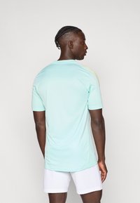 Light blue athletic shirt with short sleeves and a round neckline. Features bright yellow stripes on shoulders. Smooth fabric texture.