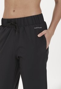 Svarta träningsoverallsbyxor i lätt material, med elastisk midja och dragsko samt sidofickor för förvaring.