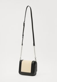 Crossbody-väska i svart läder med beige strukturerad panel; den har en avtagbar kedjesnor och rektangulär form, kompakt design.