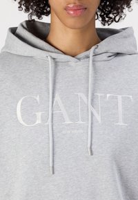 Pilkas užtrauktukas su išsiuvinėtu "GANT" logotipu ir "NEW HAVEN" detale. Turėdamas tautinę kapisoną ir lygią, švelnią tekstūrą.