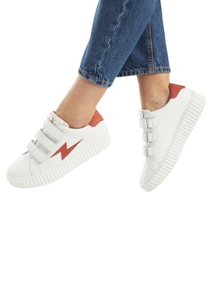 Scarpe bianche con accenti rossi, dotate di tre cinturini in velcro, una suola testurizzata e un design a forma di fulmine.