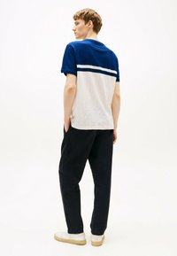 Camiseta de manga corta en azul y blanco con rayas horizontales en el pecho; combinada con pantalones negros y zapatillas blancas sobre un fondo neutro.