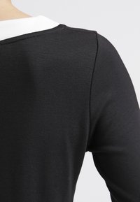 Czarna, długosleeve'owa odzież z białym kołnierzykiem, dopasowana, z gładkiego, teksturowanego materiału oraz widocznymi detalami szwów przy dekolcie.