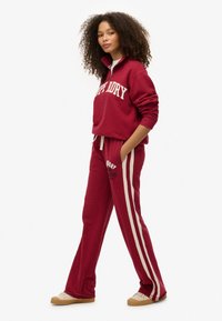 Rød bomulds sweatshirt med halv lynlås og frontlogo, parret med matchende sweatpants med sideløbe og trykt tekst.