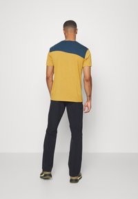 T-shirt à manches courtes avec un corps jaune moutarde et une section supérieure bleu foncé, fabriqué à partir d'un tissu doux avec une texture lisse.