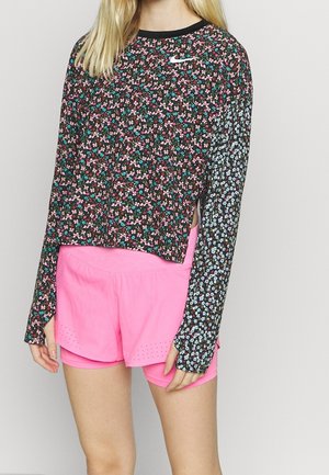 Personne portant un haut Nike à manches longues noir et rose à motif floral avec des manches contrastantes et un short de sport rose vif.