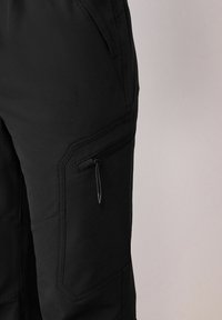 Black cargo pants featuring a smooth fabric texture, side pockets with zippers, and angular stitching details. Designed for utility and comfort.