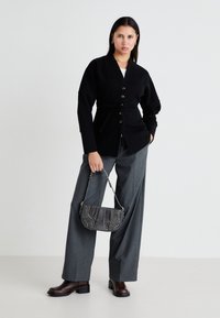Cardigã preto com cintura ajustável, fecho de botão e mangas longas. Combinado com calças largas cinzentas e uma bolsa texturizada cinzenta.