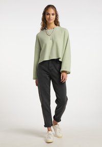 Top a maniche lunghe a coste verde chiaro abbinato a jeans neri a vita alta e sneakers bianche. Una semplice collana a strati aggiunge un tocco di dettaglio.