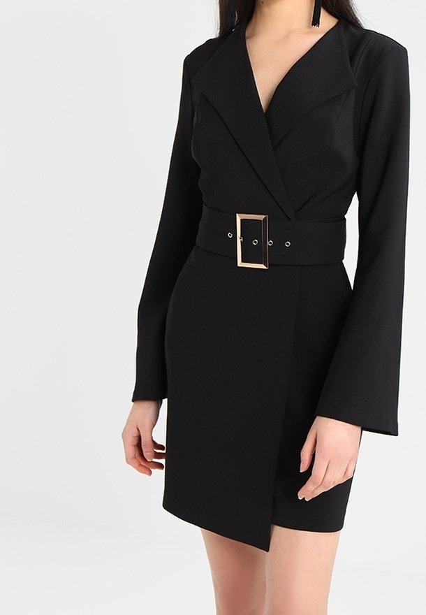 Femme portant une robe blazer noire à manches longues avec une large ceinture dotée d'une grande boucle rectangulaire.