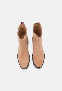 Botas de tobillo de ante color beige con paneles laterales elásticos, punta redonda y suela de goma negra. Presenta una tira de agarre a rayas en rojo, blanco y azul.