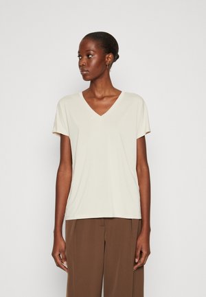 V-neck, short-sleeve, cream-colored t-shirt made of soft material, paired with loose, brown trousers. Simple design and relaxed fit.