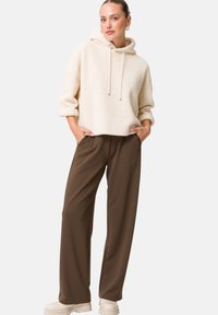 Sweatshirt à capuche crème avec une finition texturée, associé à un pantalon marron ample et des chaussures à plateforme crèmes épaisses.