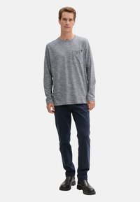 Graues Langarmshirt mit runder Ausschnitt und einer Brusttasche auf der linken Seite, kombiniert mit marineblauen Hosen und schwarzen Knöchelstiefeln. Weicher, strukturierter Stoff.