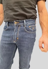 Jeans in denim blu con taglio dritto, design a cinque tasche, cuciture dorate e un'etichetta con il marchio sul retro della vita.