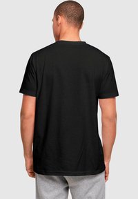Black short-sleeve t-shirt made of cotton, featuring a crew neck and a simple design without graphics or patterns, worn with gray pants.