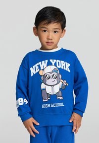 Felpa blu con un gorilla cartone animato che indossa occhiali da sole, mentre tiene una mazza da baseball. La scritta recita "NEW YORK HIGH SCHOOL" e "84" sulla manica.