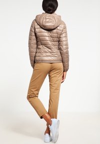 Beige puffjacka med huva, med horisontella sömmar och slät, glänsande yta. Matchad med tanfärgade byxor och vita sneakers.