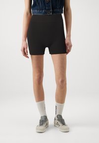 Zwarte geribbelde short met een hoge taille en een gladde textuur, gecombineerd met grijze sneakers en witte sokken met zwarte tekst.
