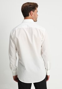 Camicia bianca con bottoni realizzata in un tessuto liscio e strutturato. Presenta un colletto classico e maniche lunghe con polsini abbottonati. Vestibilità sartoriale.