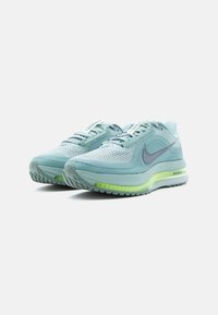 Gaiši zili Nike skriešanas apavi ar strukturētu sietu augšdaļu, zaļiem akcentiem un redzamu Air amortizāciju zolē.