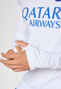 White long-sleeve shirt featuring blue "QATAR AIRWAYS" text. Material appears smooth, with fitted cuffs and minimalist design.