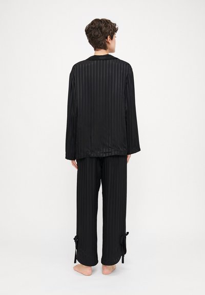 Conjunto de pijama de satén negro que presenta rayas verticales, una blusa de manga larga y pantalones con lazos en los tobillos. Textura suave y lisa.