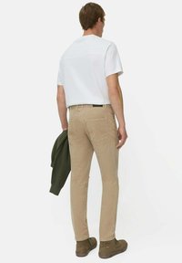 Beige Chinos mit schmaler Passform und Ges�äßtaschen, kombiniert mit einem weißen Kurzarmhemd und einer olivgrünen Jacke. braune Stiefeletten.