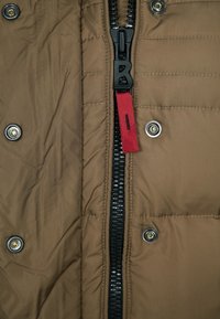 Hnědá zateplená bunda s černým předním zipem, který má červenou táhla, a čtyřmi stříbrnými patentkami na obou stranách.