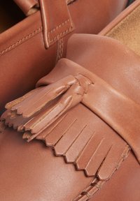 Mocassini in pelle marrone con una texture morbida, caratterizzati da un dettaglio di frangia e un design della punta liscia e arrotondata con finiture di cucitura ordinate.