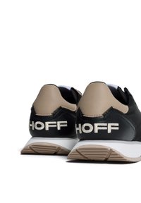 Scarpe da atletica nere e beige con tomaia testurizzata, suola bianca ammortizzata e "HOFF" ricamato in crema sul tallone.