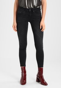 Los jeans skinny negros presentan una textura de denim suave, diseño de cinco bolsillos y se combinan con botas de tacón brillantes en color burdeos.
