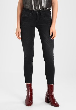Los jeans skinny negros presentan una textura de denim suave, diseño de cinco bolsillos y se combinan con botas de tacón brillantes en color burdeos.