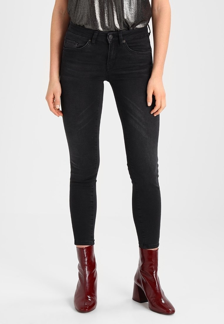 Los jeans skinny negros presentan una textura de denim suave, diseño de cinco bolsillos y se combinan con botas de tacón brillantes en color burdeos.