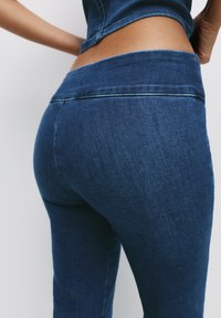 Strakke donkerblauwe denim broek met een gladde textuur en een brede tailleband. Gestikte naden zichtbaar langs de randen, die de vorm benadrukken.