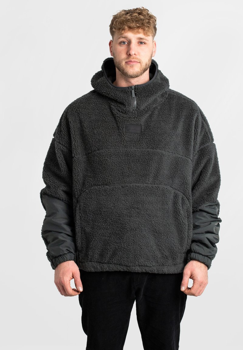 Pullover in pile con cappuccio, realizzato in materiale grigio scuro testurizzato, con zip centrale, polsini elasticizzati e un piccolo patch con logo sul petto.