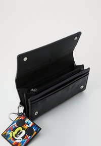 Portefeuille noir en matériau texturé, avec une poche zippée et des emplacements pour cartes, accompagné d'un porte-clés Mickey Mouse coloré.