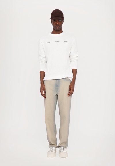 Hvit langermet skjorte med trykt tekst, lys grå jeans, hvite sneakers og en brun caps. Minimalistisk design med en avslappet passform.